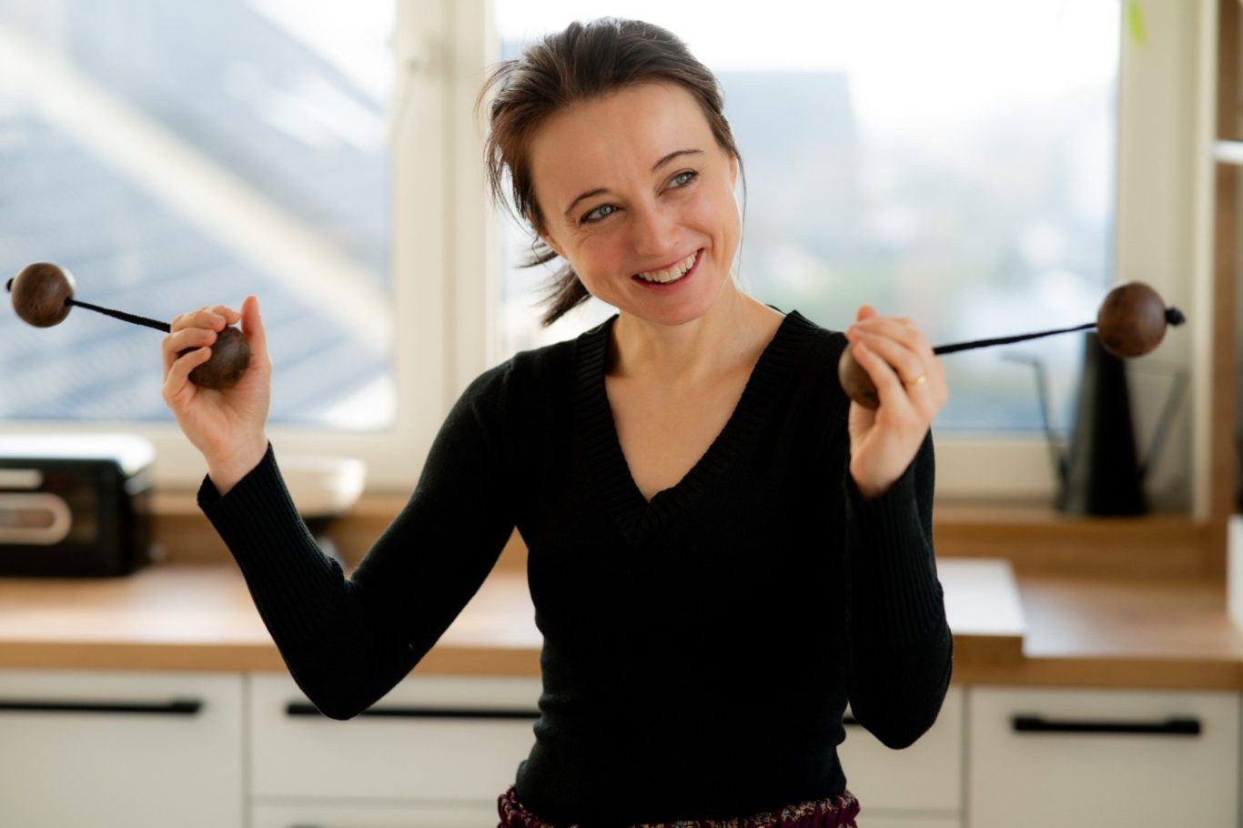 Eine Frau mit langen Haaren hält in jeder Hand ein Musikinstrument und lächelt.