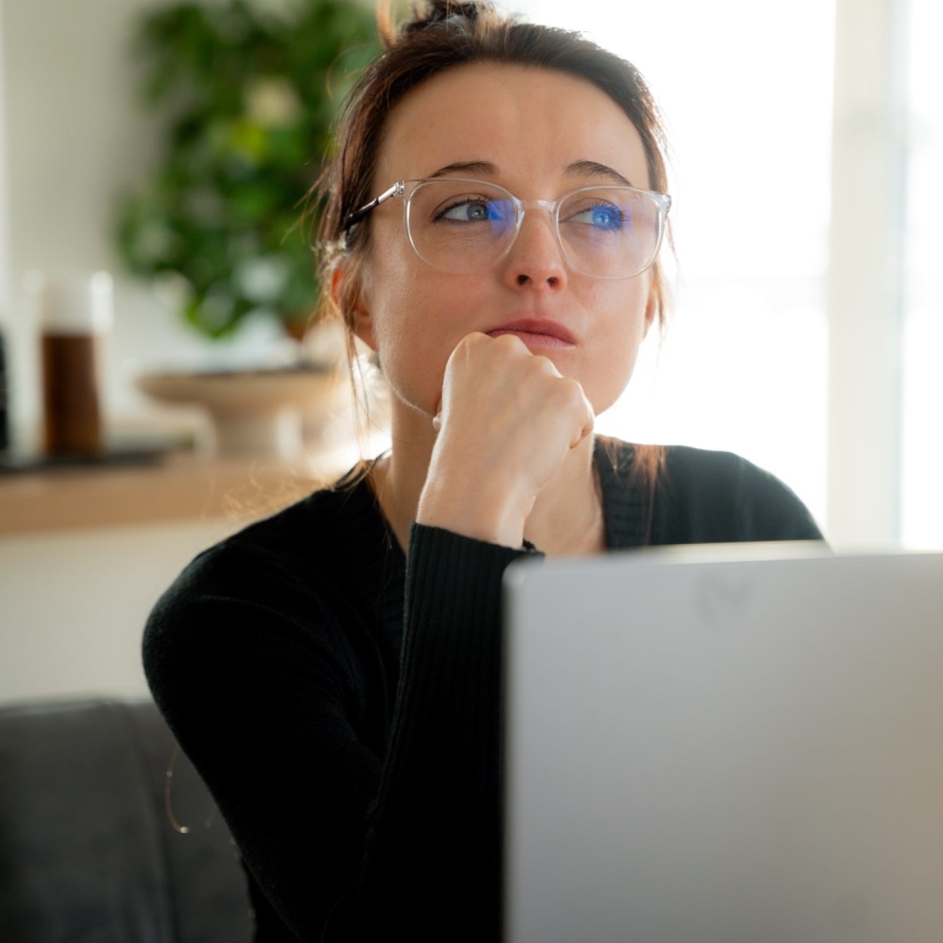 Nachdenkliche Frau mit Brille, die an einem Laptop arbeitet.